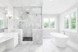 A large luxurious bathroom with a stand alone tub, white vanity, and a glass stand up shower with marble tiles and bench seat.