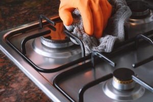 Close up view of hands in rubber gloves cleaning hob. Housework concept.