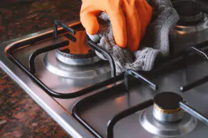 Close up view of hands in rubber gloves cleaning hob. Housework concept.